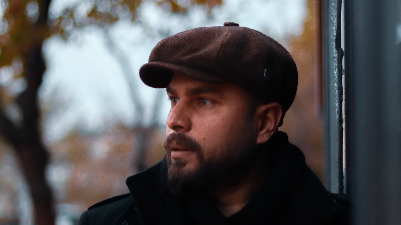 Bearded man wearing a brown newsboy cap and dark coat outdoors in autumn