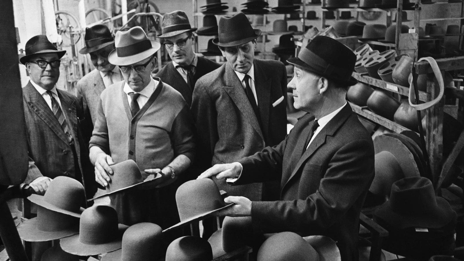 Men comparing and handling hats in a Hilversum hat shop in 1964